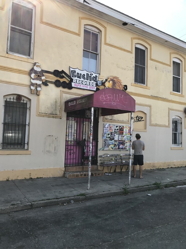 The front of a big yellow building on a street. Above the pink awning is a sign that says: Euclid Records. There's a faded Santa Clause to the left of the sign and on the right is a lion. Written on one of the sides of the pink awning says: Euclid Records. 