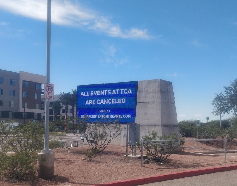 A blue sign in front of a concrete building that says ALL EVENTS AT TCA ARE CANCELED. 