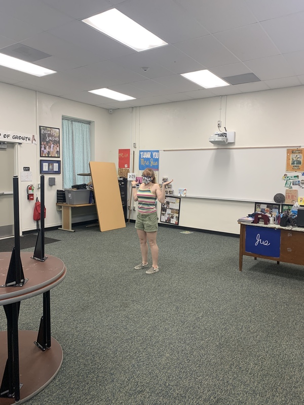 A teacher in a mask alone in a classroom. 