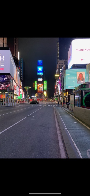 This is a picture taken of a mostly empty street, with many brightly colored electronic billboards in the background. 