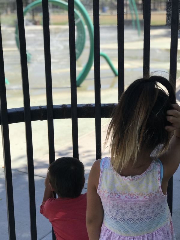 Two children looking at a closed playground through a gate.