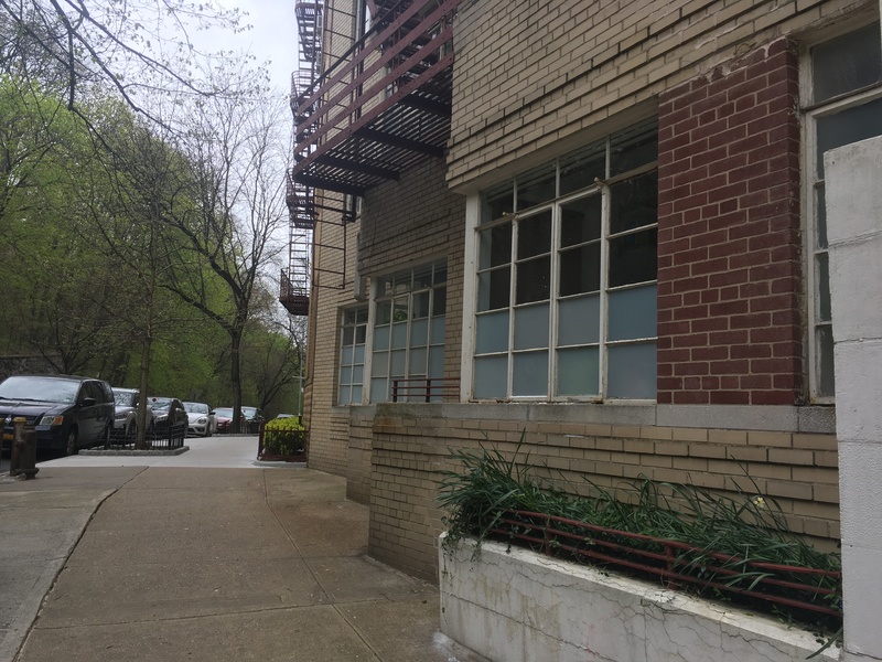 Brick buildings to the right of a walkway bordered by cars on the left.