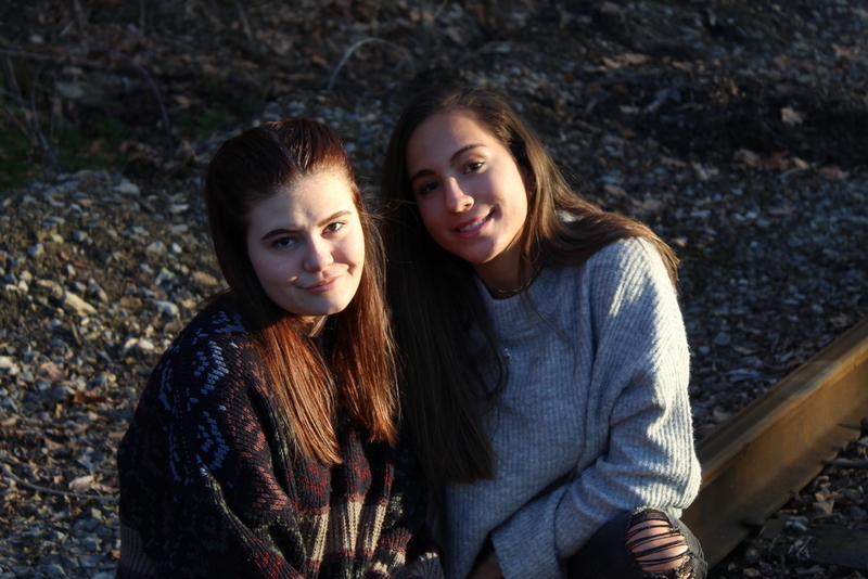 This is a picture of two women posing for a photo near a set of train tracks. 