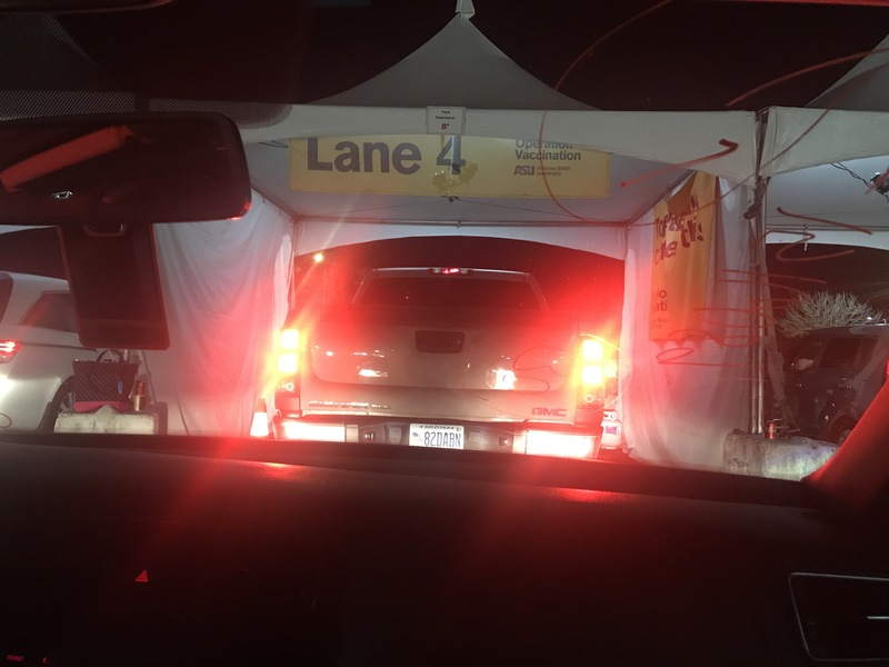 This is a picture taken from inside a car showing a line to get a vaccine at a drive in vaccination area.