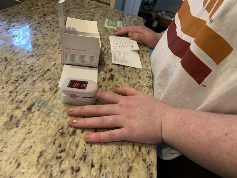 A person standing at a counter with their pointer finger in a oxygen meter. 