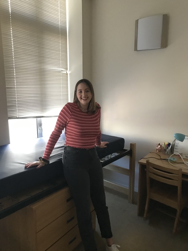 A person leaning against a bed in front of a closed window. 