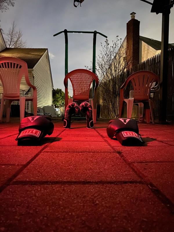 A boxing ring made out of white plastic chairs. On the ground in front of the ring is boxing gloves. 