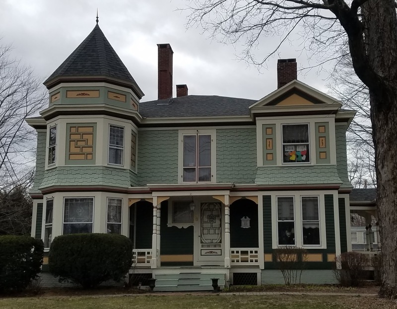 A residential house with a teddy bear in the downstair right window, and assorted colored hearts with the words "thank you" in the upstairs right window. 