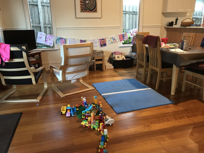 Dining/living area that has Legos on the floor, and child artwork hanging along the wall. 