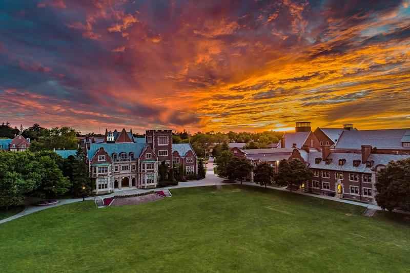 An empty campus with brown and white buildings. The sky is orange and yellow with clouds. 