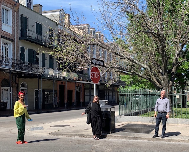 Three people are standing six feet apart from each other on the corner of a stop sign. 