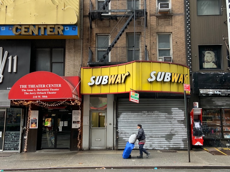 A person with bags walking in front of closed down buildings. 