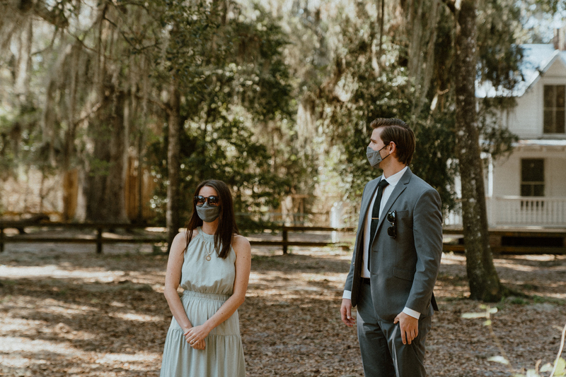 This is a picture of two people dressed in formal attire standing outside. Both are wearing face masks. 