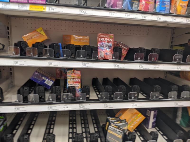 A white shelf that has multicolors of condom boxes that are yellow, blue, and red. The condom boxes have TROJAN in bold font on the front of them. 