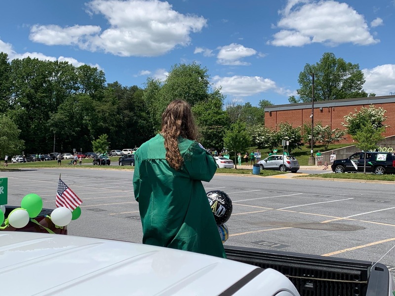 Girl in green graduation gown in front of car during graduation parade.