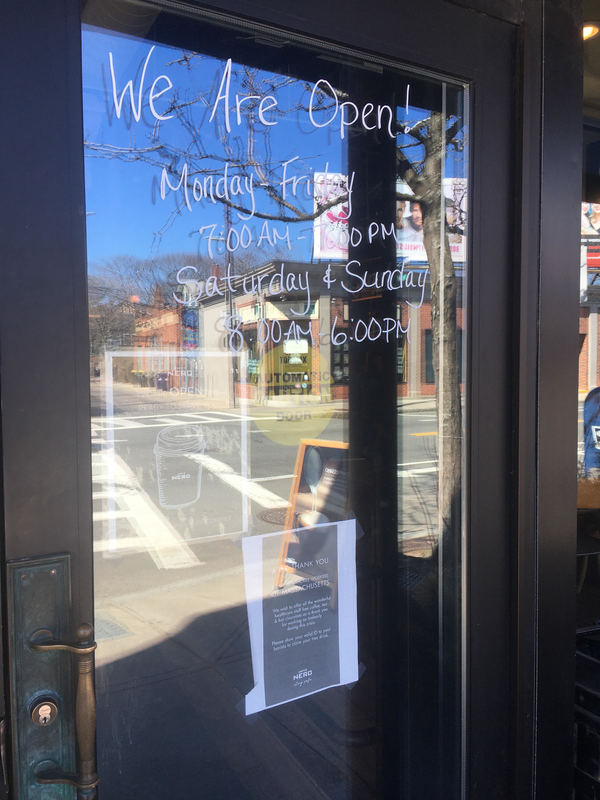 The glass front door of a café that has the hours written on it. 