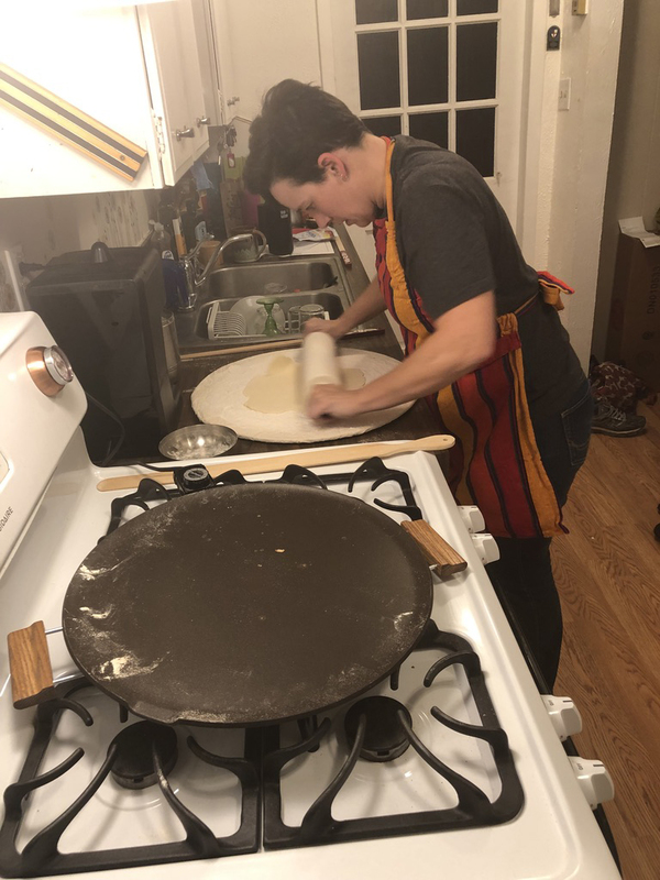 This is a picture taken of a woman rolling dough in a kitchen.