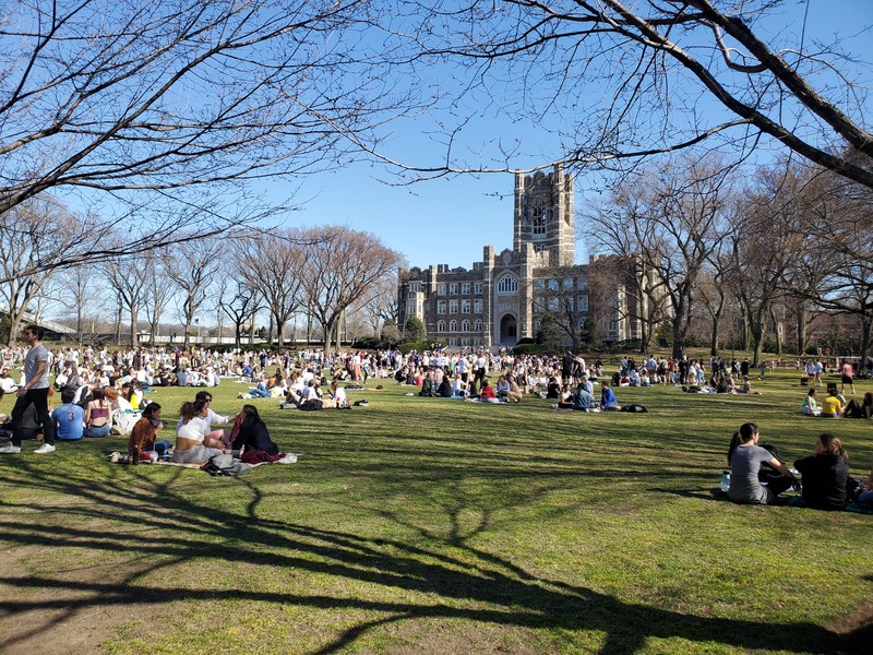 People sitting in a field in front of a building. 