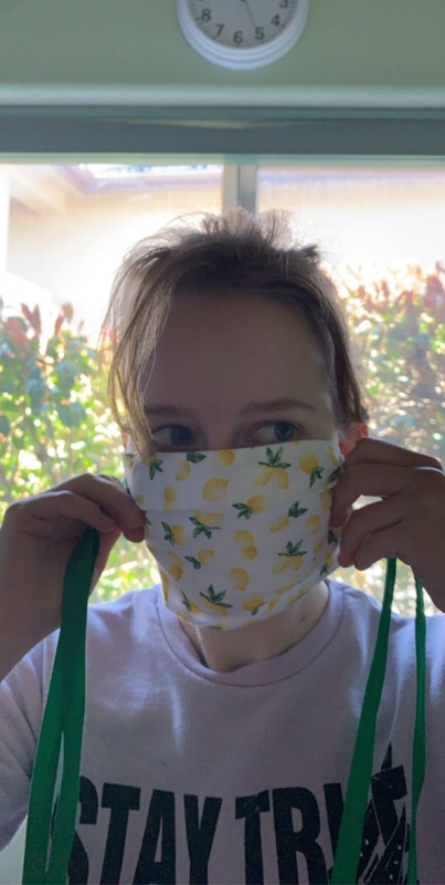 A girl holding up a handmade mask made of lemon print fabric. 