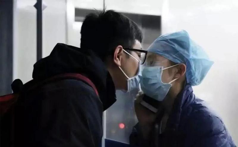 A photo of two individuals wearing masks and touching faces with glass between them.