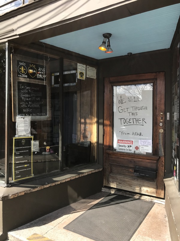 The front of a brown entrance with a glass door. On the inside of the glass door says: WE WILL GET THROUGH THIS TOGETHER *FROM AFAR.