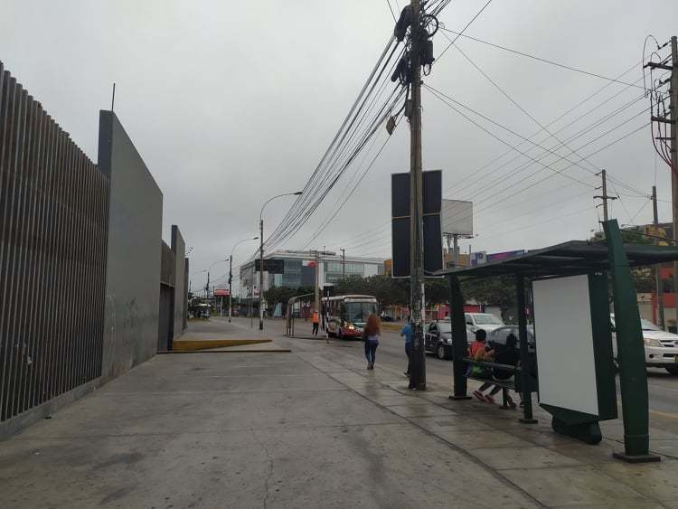 A sidewalk with few people walking on it while cars pass by. 