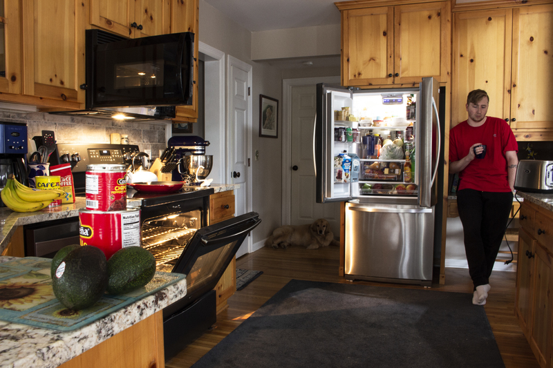 A person holding a mug surrounded by open kitchen appliances. 