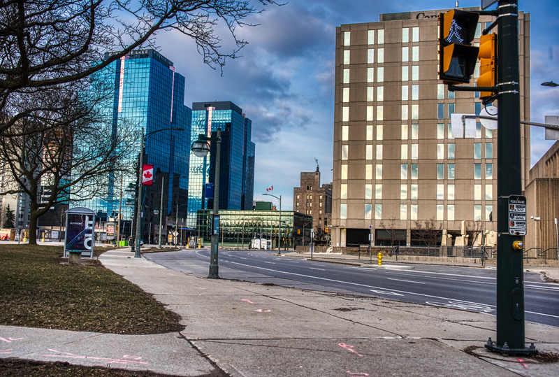 An empty street with a stop light with street lamps. Hanging from the street lamps is the Canadian flag. 