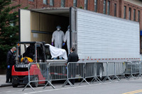 This is a picture taken of a refrigerated cadaver truck, with healthcare workers working carefully to use a forklift to deposit the remains of those who die from COVID-19. 