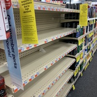 An empty row of shelves with yellow signs taped on them.