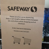 A piece of paper is taped on the front of a vending machine that talks about practicing social distancing while visiting the grocery store. 