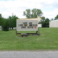 Sign with a big arrow on top with text, "LOVE GOD - LOVE ONE ANOTHER - CURE COVID 19"