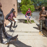 Four people talk on the sidewalk next to a car.