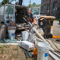 A person holding pipes behind a van.