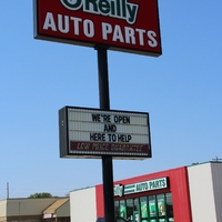 A sign outside an O'Riley's Auto Parts store reading "We're Open and Here to Help".