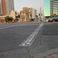 This is a picture taken of a heavily used cloth face mask lying in the gutter of a city street. Shining glass buildings are in the background. 