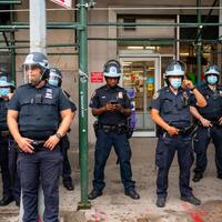 This is a picture of a group of police officers wearing both face shields and face masks standing outside of a FedEx. 