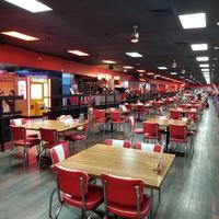 A bowling alley with empty red and white tables and chairs going off into the distance. 