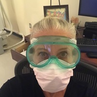 A woman working at a medical center wearing goggles and two masks. 