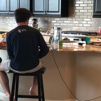 A young man sitting at a kitchen counter attending a virtual orientation for University.