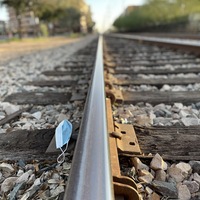 This is a picture of a discarded cloth mask resting on a series of train tracks. 