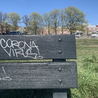 white graffiti on a black bench saying "corona virus"