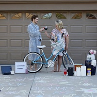 Two people posing behind toiletries and a laptop in front of their garage. 