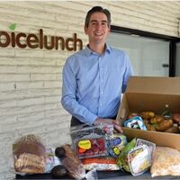 A man posing with a box of food displayed on a table.