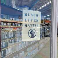 This is a picture of a sign in a storefront window which reads "Black Lives Matter", followed by the Black Power Movement symbol of a raised fist. 