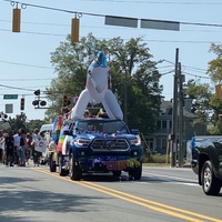 This is a picture of an inflated unicorn attached to the back of a truck, which is taking part in a Pride Parade celebrating LGBTQ culture. 