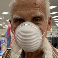 An older man with his beard falling out from a mask.