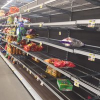 An aisle in a grocery store that has barely stocked bags of chips on the shelves. 