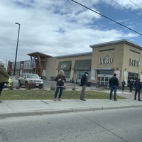 Image of a line of people standing outside social distancing.