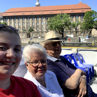 This is a picture taken of three people sitting outside and smiling for a picture. A younger woman is seated next to an older women and an older man. 